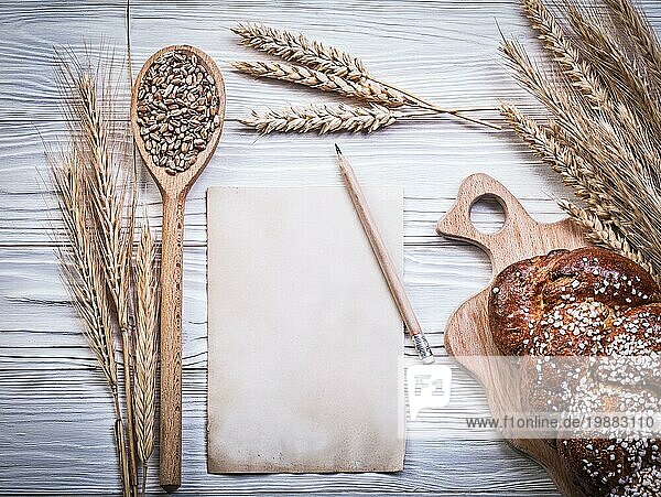 Komposition von Carving Board Weizen Rye Ohren gebacken Brot Stock Holzlöffel Korn Vintage Papier Blatt Bleistift