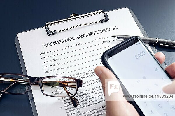 Blank Student Loan Application auf dem Tisch und Hand hält ein Smartphone mit Taschenrechner App. Bildungskosten