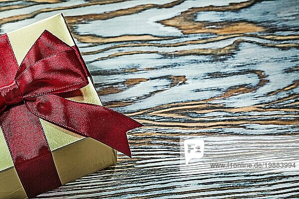 Goldene Geschenkbox mit rotem Knoten auf Holzbrett