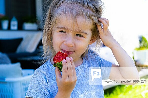 Kleines blondes lockiges Mädchen ißt frische Erdbeeren im Hinterhof