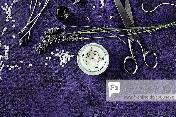 Handgefertigte Lavendelduftkerze mit ätherischem Öl  Blumen  Wachs  Dochten und Scheren  eine flache Overhead Aufnahme auf einem dunkelvioletten Hintergrund mit Platz für Text