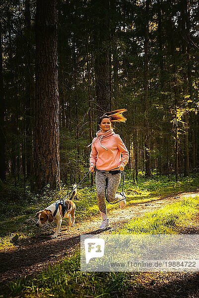 Junge Frau und Hund laufen zusammen auf dem Land im Wald. Fröhliche Frau  die mit ihrem Haustier im Freien trainiert. Aktive Menschen Konzept