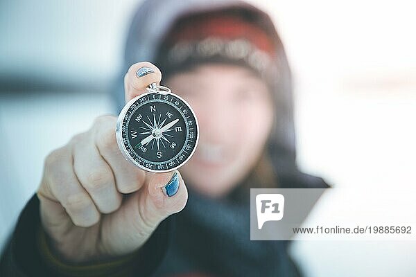Junge lächelnde Frau hält einen Kompass hoch. Winterzeit  Handschuhe und Kapuze