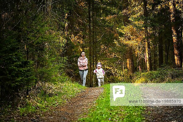 Junge Frau mit 2 Jahre alten Tochter zusammen läuft auf dem Land im Wald. Fröhliche Frau trainiert mit ihrem Kind im Freien. Aktive Menschen Konzept