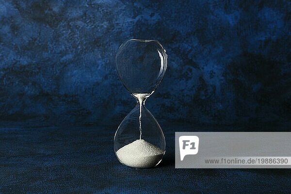 Die Zeit läuft aus Konzept. Eine Sanduhr mit Sand fallen durch  auf einem dunkelblauen Hintergrund mit einem Platz für Text