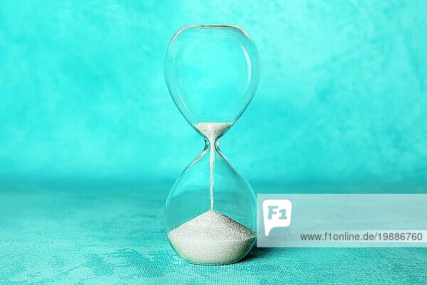 Die Zeit läuft aus Konzept. Eine Sanduhr mit Sand fallen durch  auf einem leuchtend blaün Hintergrund mit einem Platz für Text