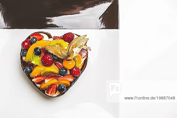 Herzförmige Fruchtbiskuit  Obsttorte auf einem quadratischen Teller auf dem Tisch. Gesunde Süßwaren Hintergrund. Platz für Text