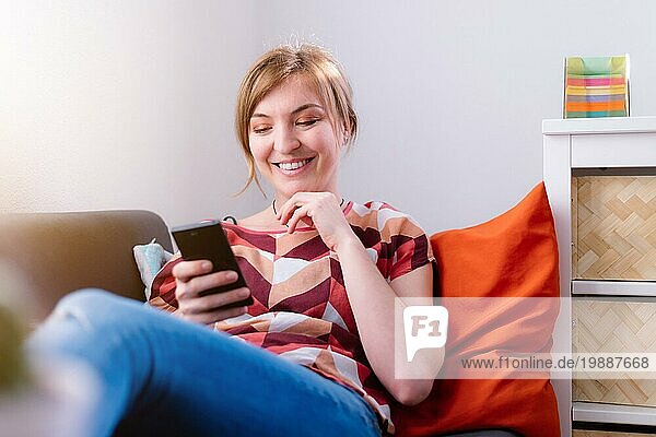 Blondes attraktives Mädchen liegt auf dem Sofa und schreibt SMS mit ihrem Freund