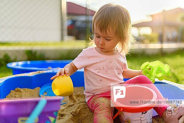 Baby Mädchen spielt in einem Sandkasten im Freien in sonnigen Tag. Kind im blaün Sandkasten im Sommer