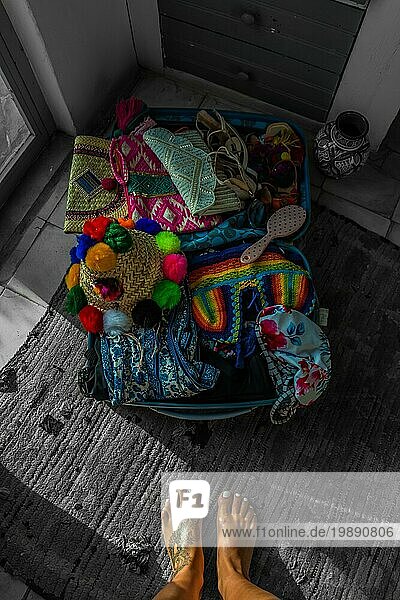 Ein Bild eines mit bunten Gegenständen gefüllten Koffers zu den Füssen einer Person