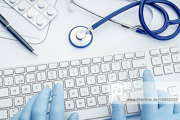 Arzt Hände in Handschuhen Tippen auf Computertastatur auf weißem Schreibtisch. Telemedizin oder Medizintechnik Konzept Hintergrund. Ansicht von oben