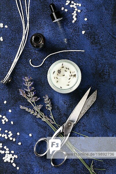 Handgemachte Lavendelduftkerze mit ätherischem Öl  Blumen  Wachs  Dochten und Schere  flach gelegt  Overhead Aufnahme auf dunklem Hintergrund. Ein handwerkliches Weihnachtsgeschenk
