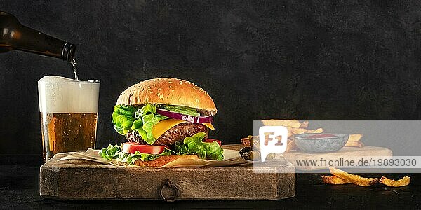 Burger und Bier Panorama. Hamburger mit Rindfleisch  Käse  Zwiebel  Tomate und grünem Salat  eine Seitenansicht auf einem dunklen Hintergrund mit einem Platz für Text. Selektiver Fokus
