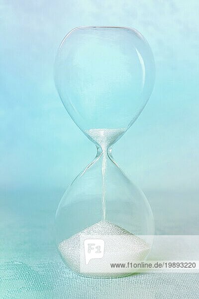 Zeit Konzept. Eine Sanduhr auf einem abstrakten Hintergrund  durch den Sand sickert. Blau getöntes Bild