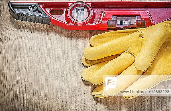 Gelbe Handschuhe und rote Wasserwaage auf Holzplatte