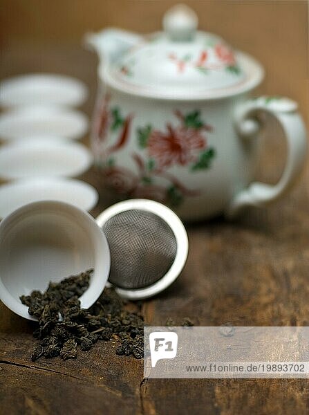 Trockenes grünes chinesisches Teeset mit Sieb in Großaufnahme  Tassen und Teekanne im Hintergrund auf altem Holzbrett  Food photography