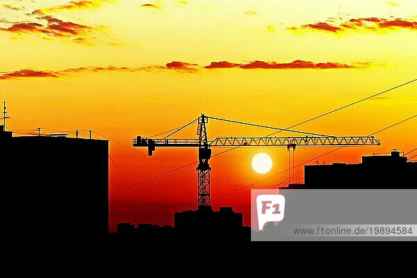 Silhouetten von Häusern und Baukran gegen die untergehende Sonne  Skyline der Stadt bei Sonnenuntergang