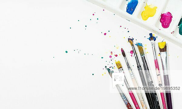 Art Paint Pinsel und Palette mit bunten Farbspritzern auf weißem Leinwandpapier. Kopierraum