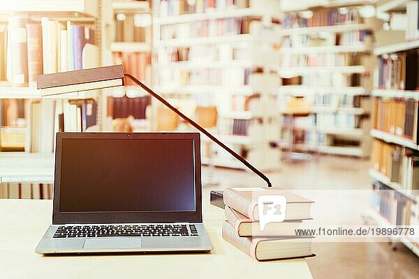 Laptop und Stapel von Büchern auf einem Holztisch. Universitätsbibliothek