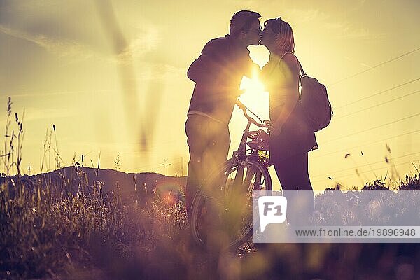 Junges Paar mit Fahrrad küsst sich auf einem Feld  Sonnenuntergang