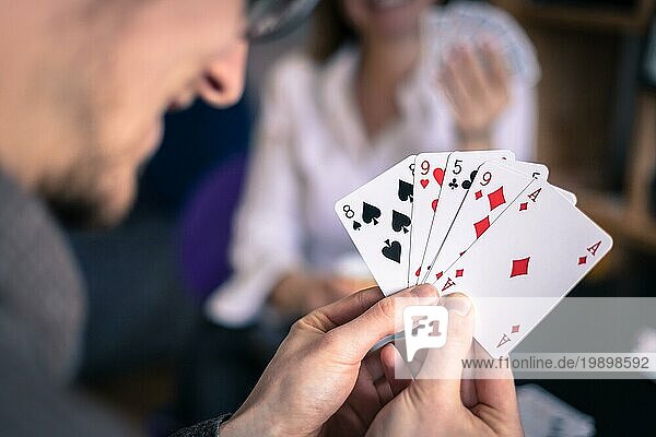 Kartenspielen zu Hause: Freunde sitzen an einem Tisch. Mann spielt Karten  Mann im unscharfen Hintergrund