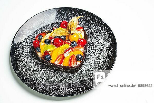 Herzförmiger Fruchtbiskuit  Obsttorte auf schwarzem Teller mit Puderzucker bestreut. Gesunde Süßwaren Hintergrund. Kopieren Raum