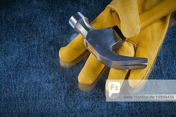 Lederschutzhandschuh mit Klauenhammer auf zerkratztem metallischem Hintergrund Konstruktionskonzept