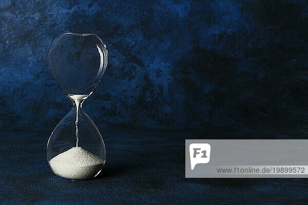 Die Zeit läuft ab Konzept. Eine Sanduhr mit Sand fallen durch  auf einem dunkelblauen Hintergrund mit Kopie Raum