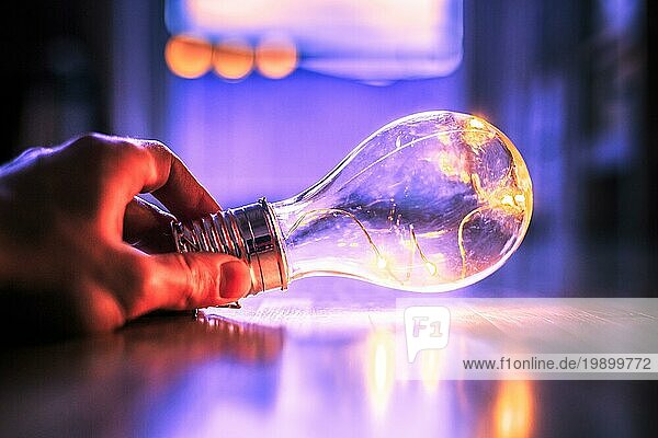 Die Hände halten eine LEDglühbirne über dem Holzboden. Symbol für Ideen und Innovation. Fenster und Licht im unscharfen Hintergrund