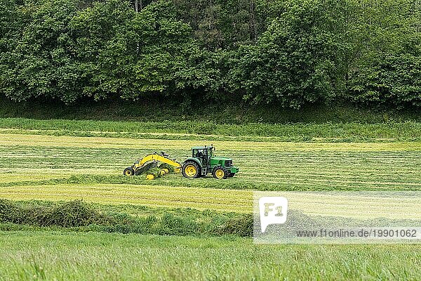 Schöne ländliche Szene mit einem Traktor und Maschinen  die das gemähte Gras auf einem landwirtschaftlichen Feld ernten. Weiden für Tierfutter
