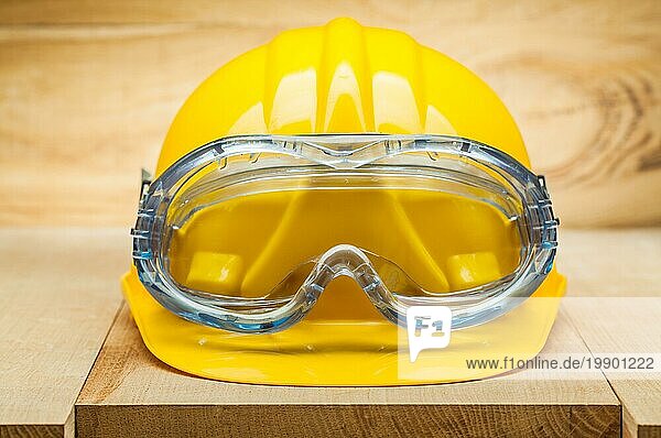 Sicherheitswerkzeuge. Gelber Bauhelm mit blaür Schutzbrille auf Holzbrett