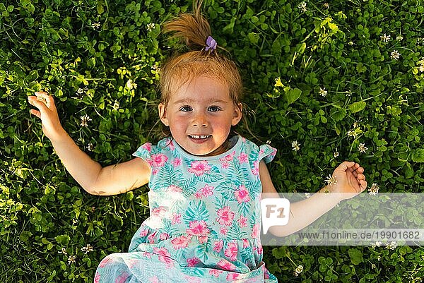 Junges Mädchen liegt lachend im Gras und schaut nach oben. 23 Jahre altes Kind in der Natur an einem sonnigen Sommertag