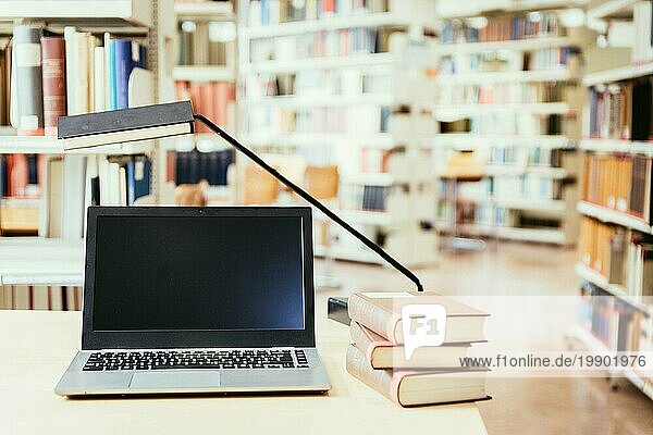 Laptop und Stapel von Büchern auf einem Holztisch. Universitätsbibliothek