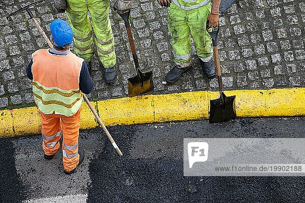 Unbekannte Bauarbeiter bei Asphaltierungsarbeiten auf einer Stadtstraße. Asphaltierung. Hohe Winkelansicht