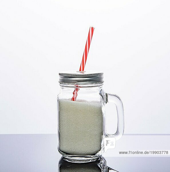 Glasgefäß mit rotem Strohhalm voller Zucker. vor weißem Hintergrund. Zucker Getränk Konzept
