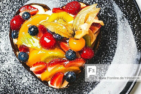Herzförmiger Fruchtbiskuit  Obsttorte auf schwarzem Teller mit Puderzucker bestreut. Gesunde Süßwaren Hintergrund