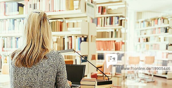 Blonde Studentin sitzt am Schreibtisch mit Stapel von Büchern  Universitätsbibliothek