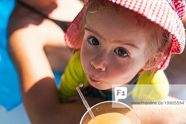 Niedliches kleines Mädchen trinkt draußen Saft mit einem Strohhalm. Baby im Sommer Thema