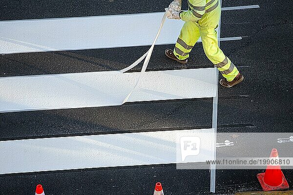 Arbeiter beim Entfernen von Abdeckband nach dem Anbringen eines Zebrastreifens auf einer städtischen Straße