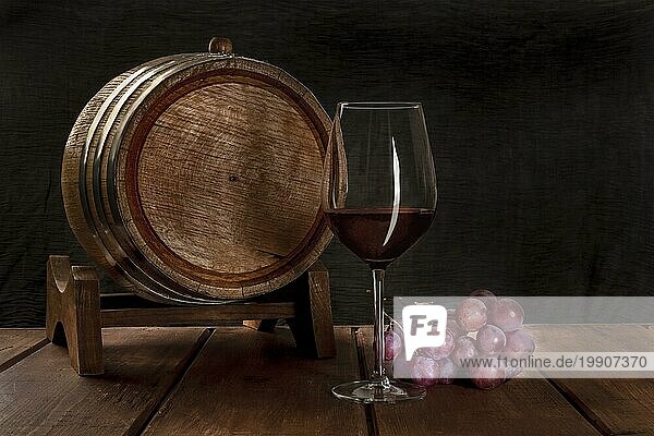Ein Glas Rotwein mit einem Weinfass und Trauben auf einem dunklen rustikalen Hintergrund  Low Key Foto mit copyspace