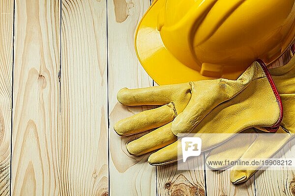 Handschuhe und gelber Bauhelm auf Holz