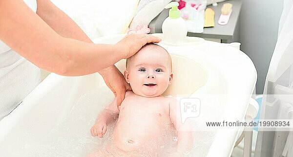 Bezauberndes kleines Mädchen in der Badewanne mit Mutter. Sie schaut mit großen braunen Augen auf und lächelt. Leerzeichen kopieren