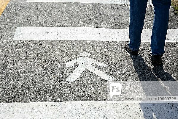 Fußgängerzeichen auf dem Asphalt und menschliche Beine zu Fuß auf sonnigen Tag