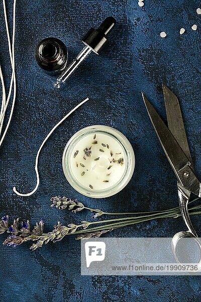 Handgemachte Lavendelduftkerze mit ätherischem Lavendelöl  Blumen  Wachs  Dochten und Scheren  eine flache Overhead Aufnahme auf einem dunklen Hintergrund. Ein handwerkliches Neujahrsgeschenk  ein Zero Waste Weihnachtskonzept