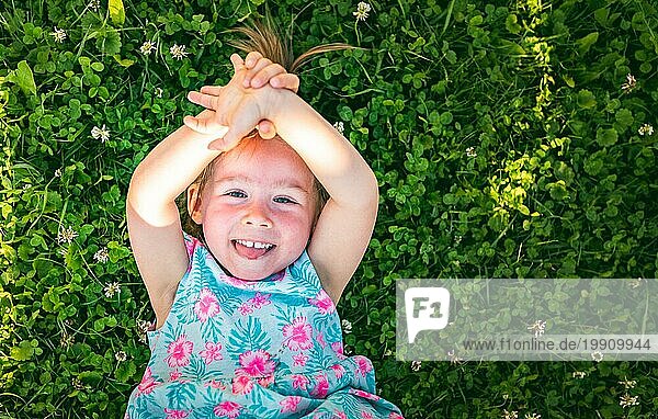 Schönes kleines Mädchen liegt im Gras und lacht und schaut nach oben. 23 Jahre altes Kind in der Natur an einem sonnigen Sommertag