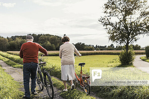 Senior couple with bicycles walking on footpath in field