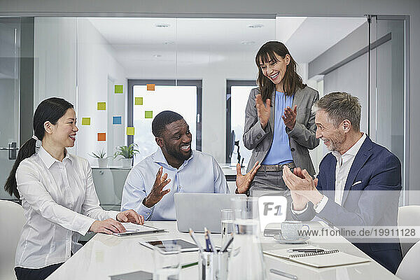 Happy businessman discussing with colleagues applauding at desk in office