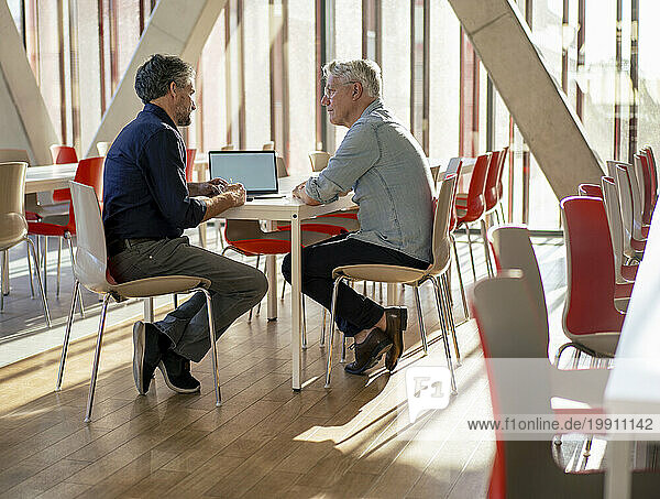 Senior businessman discussing with colleague over laptop at table in cafeteria