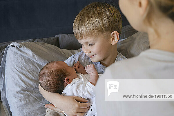 Mother with son holding baby boy on bed at home