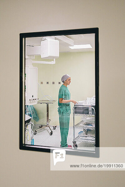 Nurse in operating room seen through glass window